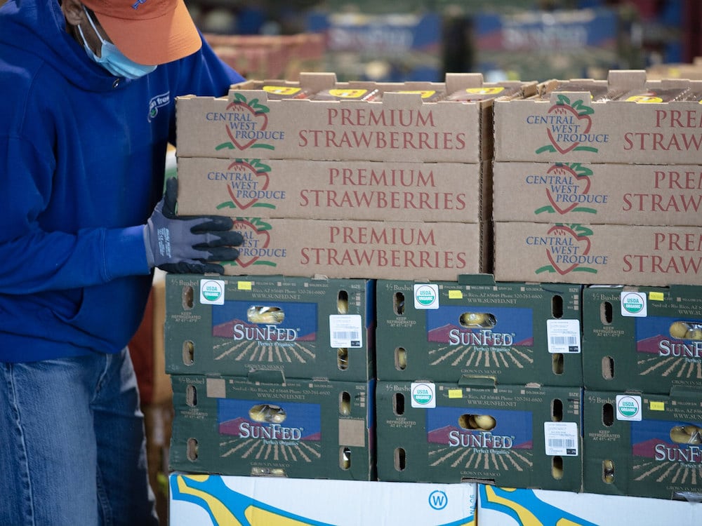 Person stacking boxes of strawberries and other produce