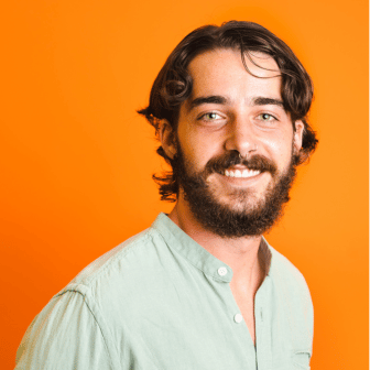 Diego in green shirt smiling in front of orange background