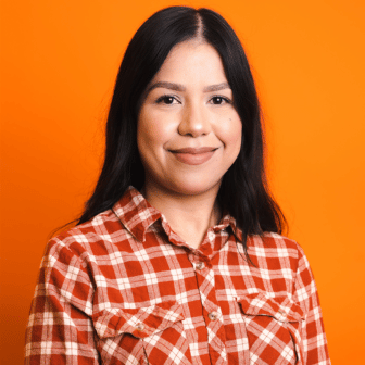 Pearl smiling in red plaid shirt in front of orange background
