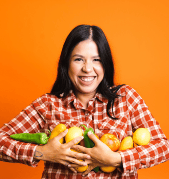 Pearl holding various fruits and smiling in front of orange background