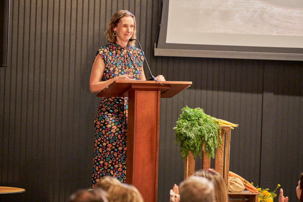 emily parker addresses the audience from a podium at food forward’s tomorrow’s table event.