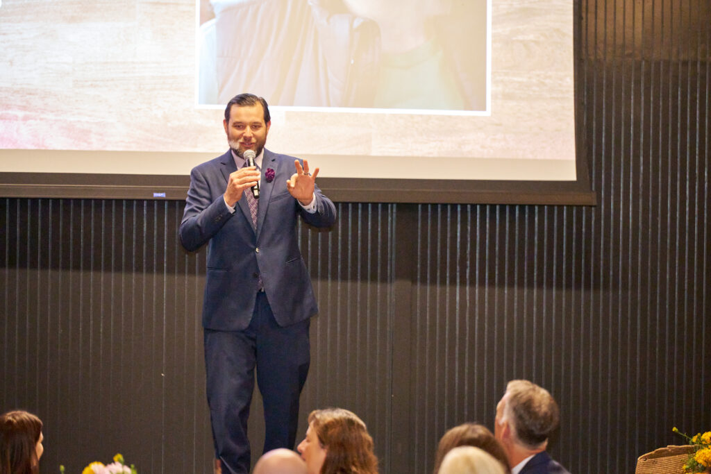 a speaker with a microphone addresses guests at food forward’s tomorrow’s table event.