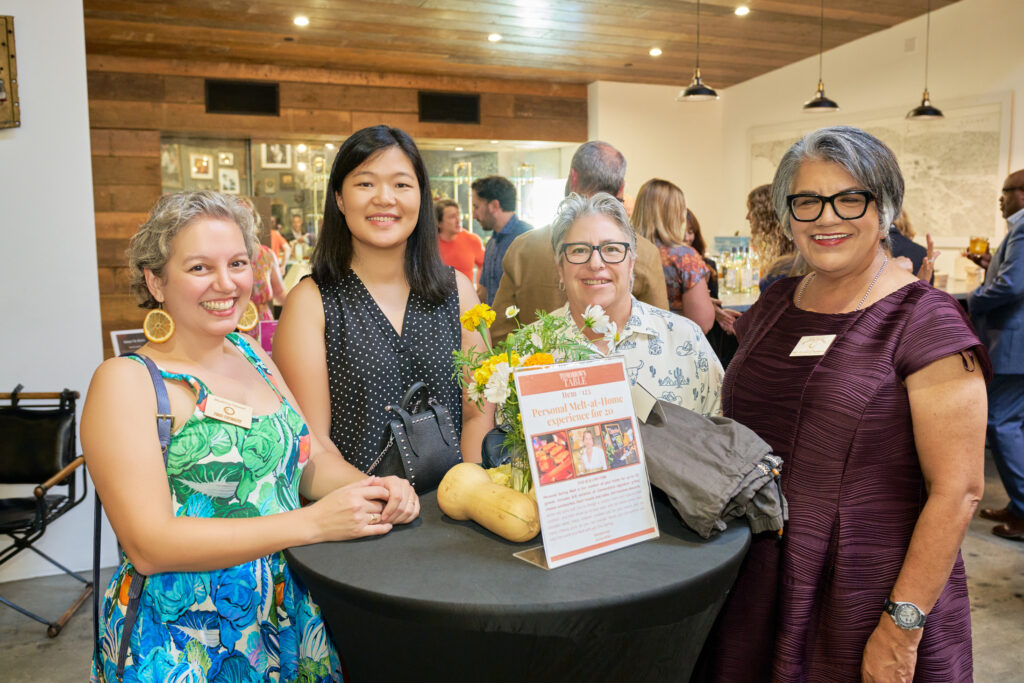 four guests pose beside a live auction item sign at food forward’s tomorrow’s table event.